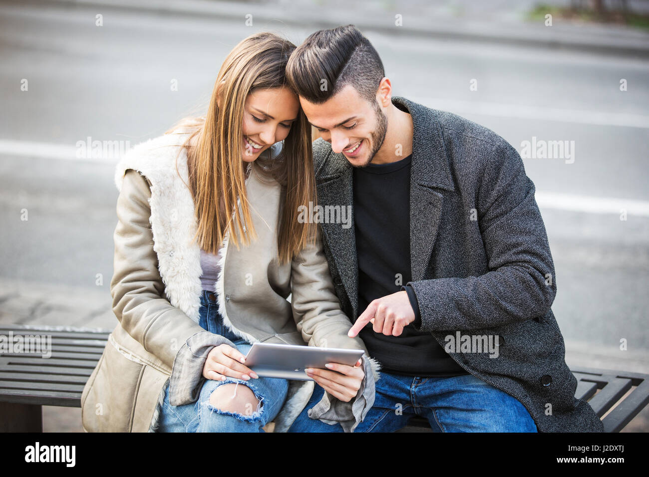 Porträt der schönen Smilling junges Paar mit einem digital-Tablette und genießen zusammen, auf einer Bank sitzen. Moderne Beziehung Konzept. Surfen Stockfoto