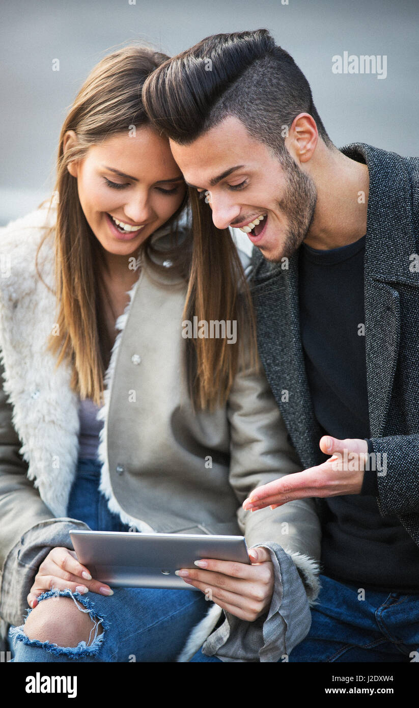 Porträt der schönen Smilling junges Paar mit einem digital-Tablette und genießen zusammen, auf einer Bank sitzen. Moderne Beziehung Konzept. Surfen. Stockfoto