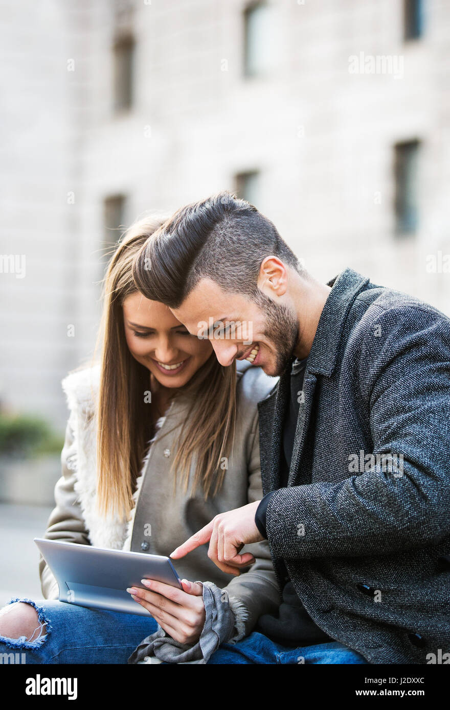 Porträt der schönen Smilling junges Paar mit einem digital-Tablette und genießen zusammen, auf einer Bank sitzen. Moderne Beziehung Konzept. Surfen. Stockfoto