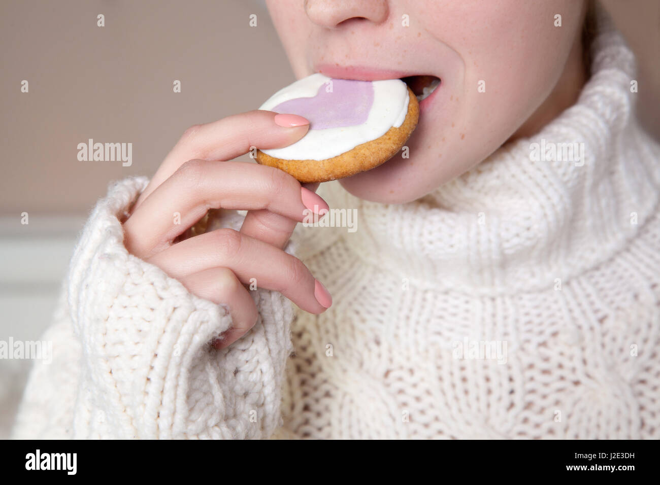 Mädchen beißt Scheibe Biskuit. Nahaufnahme der Frau mit weißer Pullover Keks in den Mund zu halten. Stockfoto