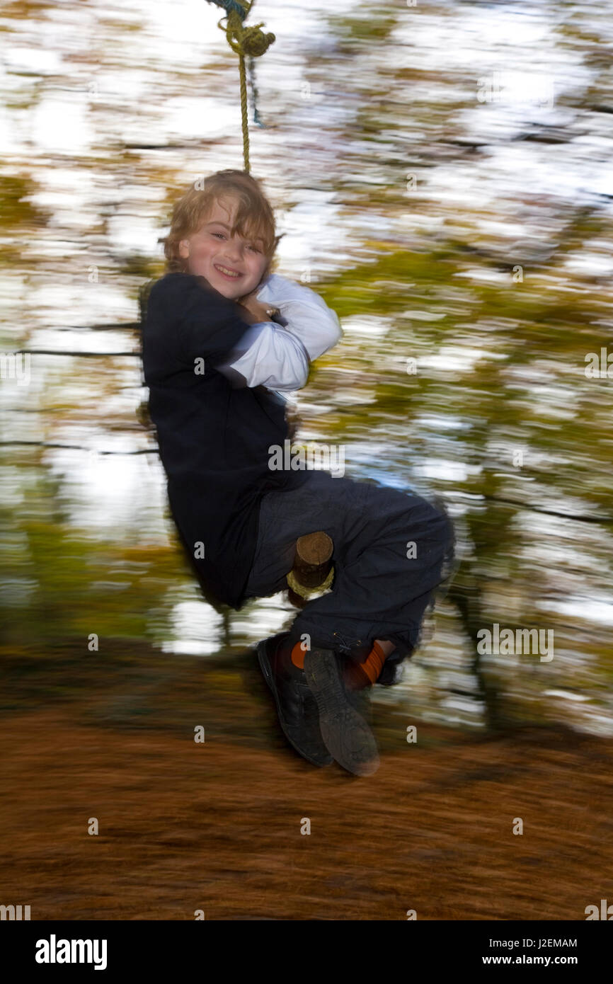 9-jähriger Junge auf Schaukel im herbstlichen Wald, Gloucestershire, England UK Stockfoto