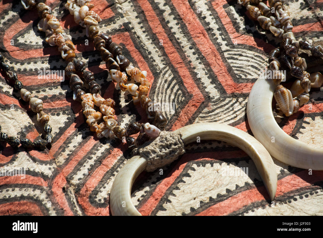 Papua Neu Guinea, Tufi. Muschelketten mit Wildschwein Stoßzähne auf traditionelle Handarbeit Tapa Tuch, gemacht vom Papier Maulbeerbaum, von hand bemalt mit natürlichen Farbstoffen, die mit geometrischen Mustern unverwechselbar, jedes Dorf. Stockfoto