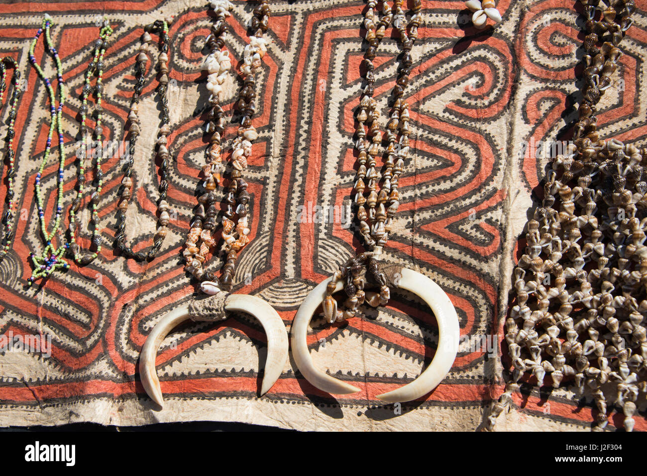 Papua Neu Guinea, Tufi. Muschelketten mit Wildschwein Stoßzähne auf traditionelle Handarbeit Tapa Tuch, gemacht vom Papier Maulbeerbaum, von hand bemalt mit natürlichen Farbstoffen, die mit geometrischen Mustern unverwechselbar, jedes Dorf. (Großformatige Größen erhältlich) Stockfoto