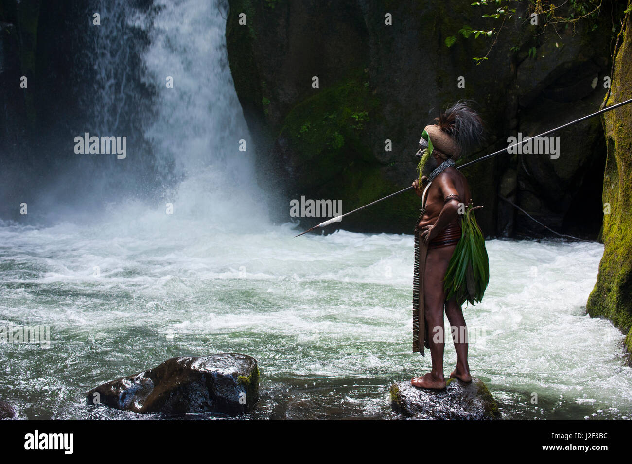 Bunt gekleidet und bemalten lokalen Stammes-Leiter steht vor einem Wasserfall in das Hochland von Papua-Neuguinea, Melanesien Stockfoto