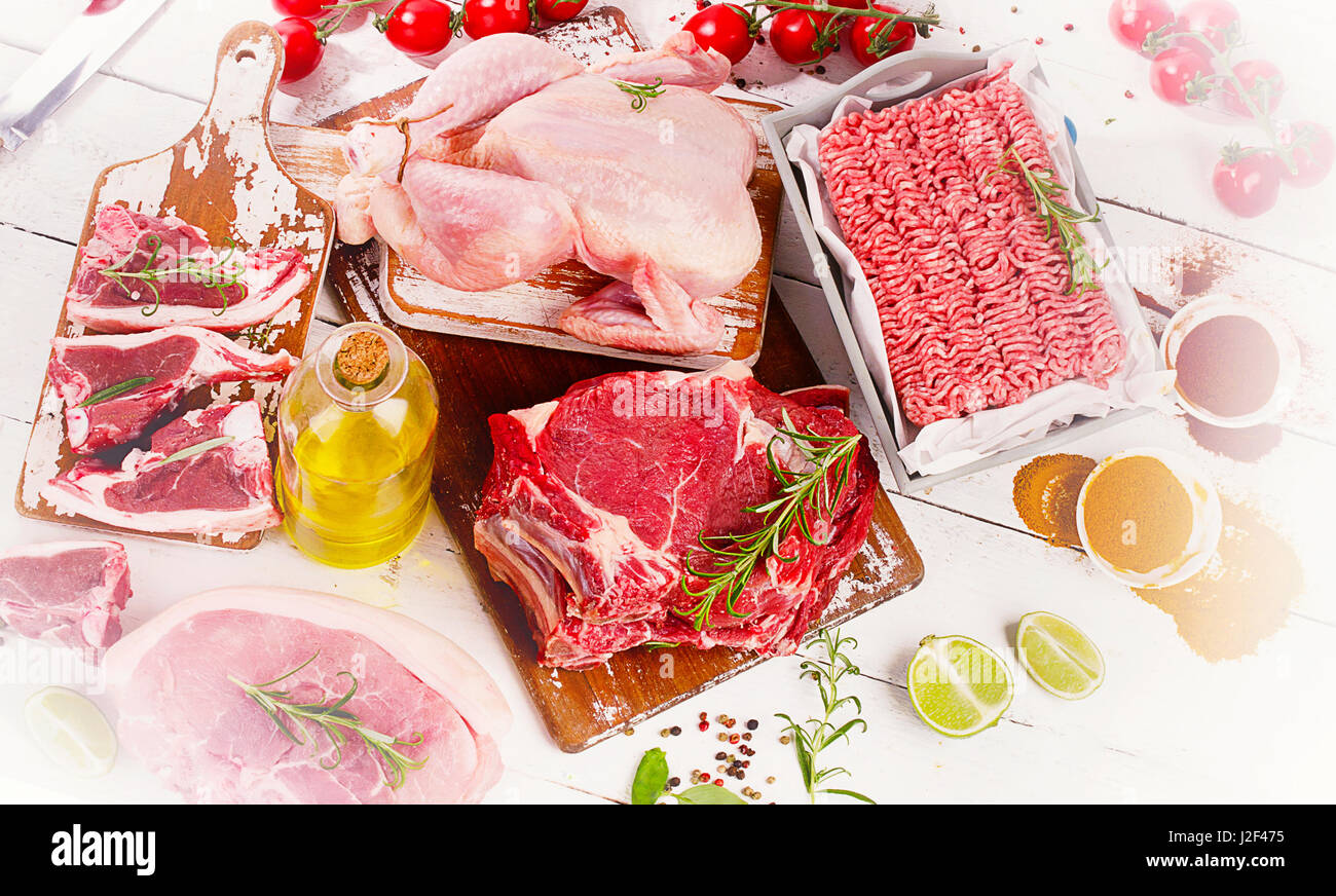 Verschiedene Arten von rohem Fleisch mit frischem Gemüse, Kräutern und Gewürzen. Ansicht von oben Stockfoto