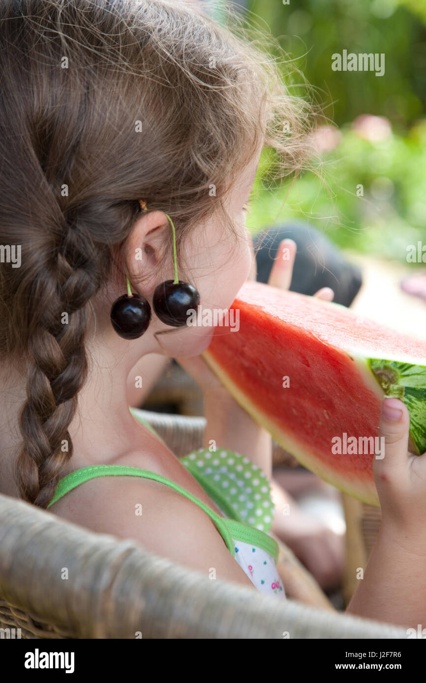 Mädchen mit Zopf und Kirschen essen Melone. Modell veröffentlicht Stockfoto