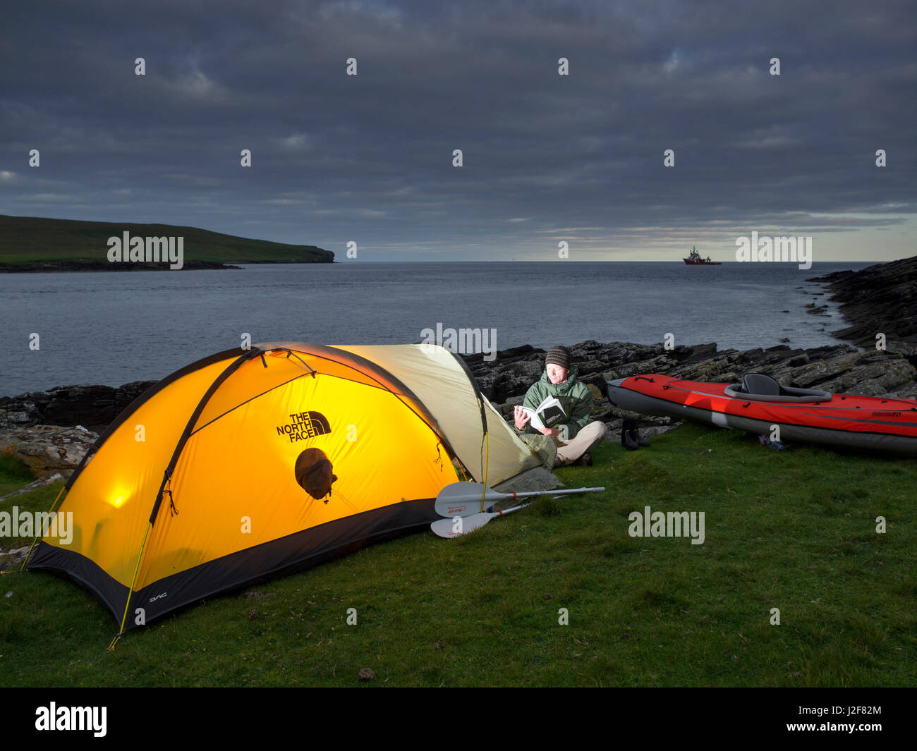 Mann mit Kajak camping. Der Blick auf die Gannet Insel Noss und ein Schiff auf der Nordsee. Shetland-Inseln, Schottland. Stockfoto