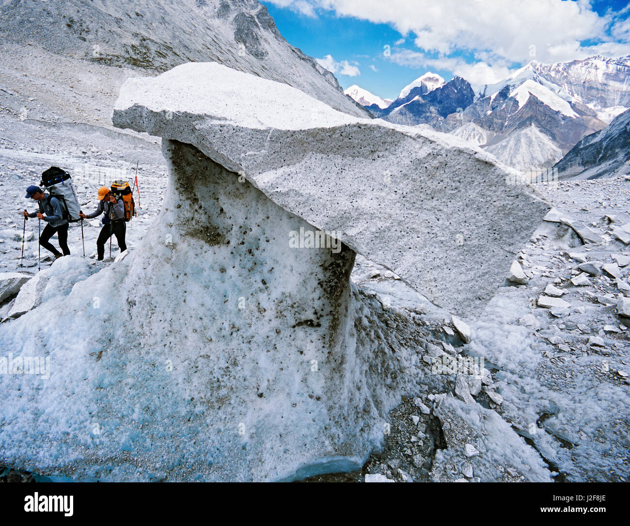 Zwei Bergsteiger ein Steintisch oder Gletschertisch vorbei. Dies ist ein Zeichen für eine schnelle schmelzenden Gletscher. Die Stein werden unterstützt durch eine Spalte des Eises, die langsamer als das umgebende Eis durch die Schatten des Steins schmilzt. Stockfoto