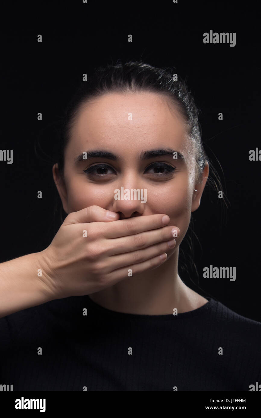 eine junge Frau, Hand, Mund, Lächeln, schwarze Kleidung, Blick auf die Kamera, schwarzer Hintergrund Stockfoto