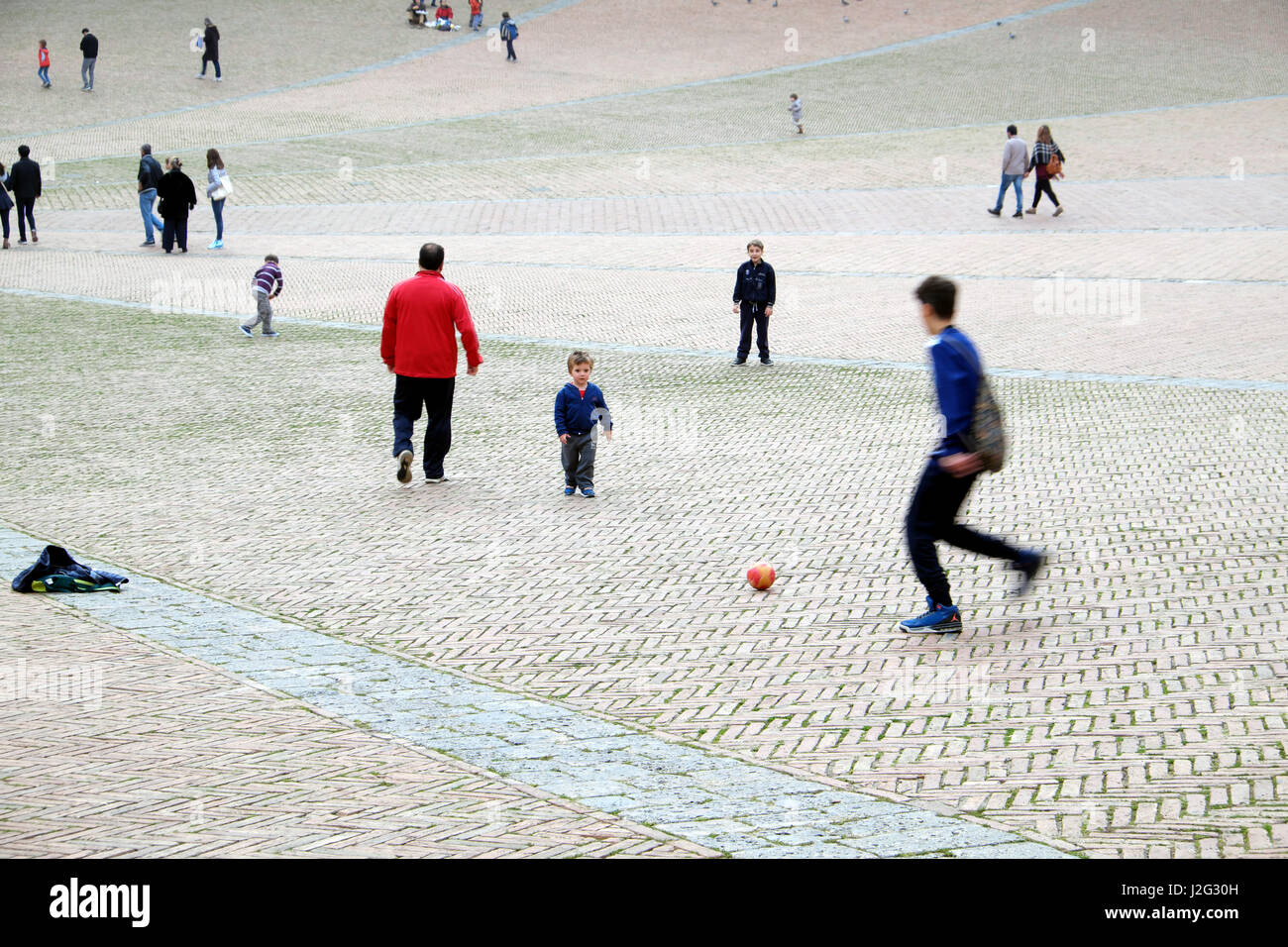 Straßenfußball - jungen und Kind spielt Fußball (Fußball) im italienischen historischen Platz - Menschen im Hintergrund - Piazza del Campo, Siena, Italien Stockfoto