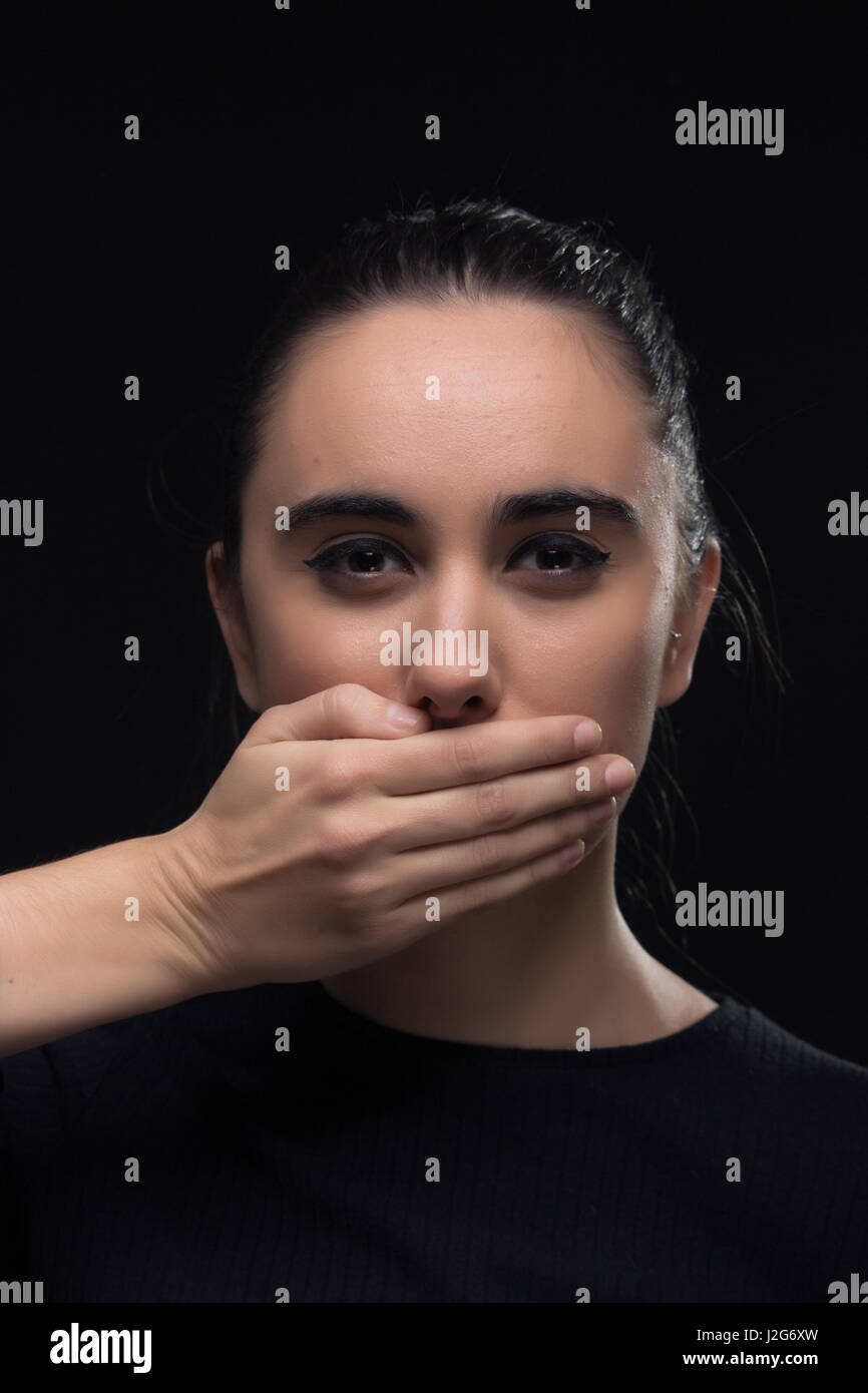 eine junge Frau, die hand für Mund, schwarze Kleidung, Blick in die Kamera, schwarzer Hintergrund, Augen Schielen Stockfoto