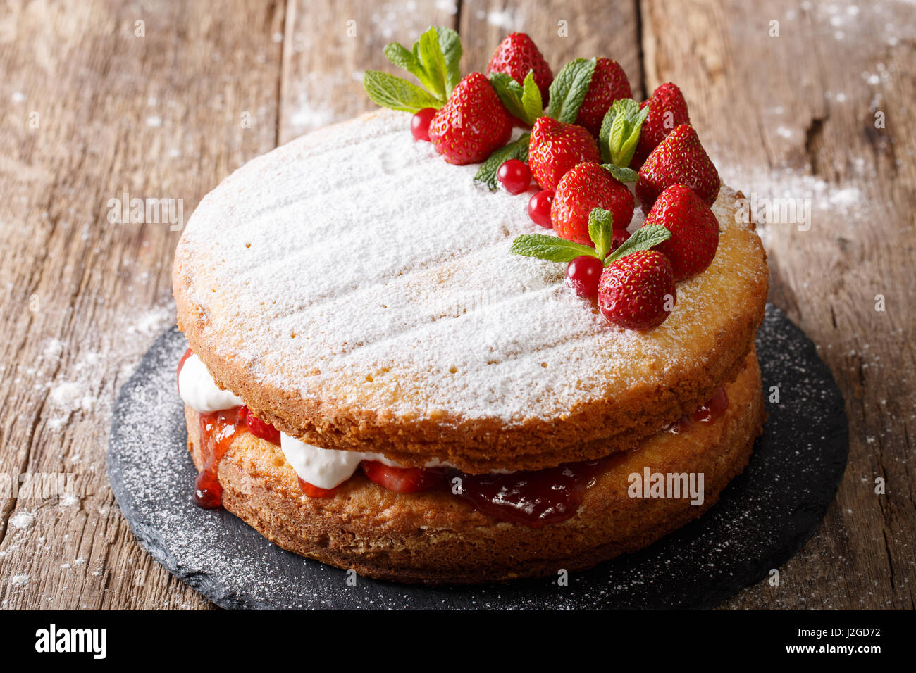 Victoria-Biskuit, dekoriert mit Erdbeeren, Preiselbeeren und Minze Closeup auf dem Tisch zu Hause. Horizontale Stockfoto