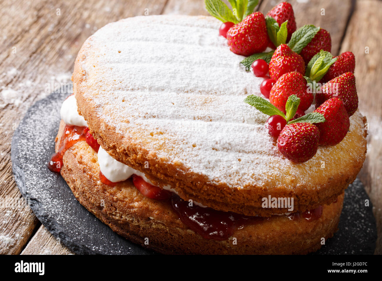 ganzen Victoria Sandwich Kuchen, dekoriert mit Erdbeeren, Preiselbeeren und Minze Closeup auf dem Tisch. horizontale Stockfoto