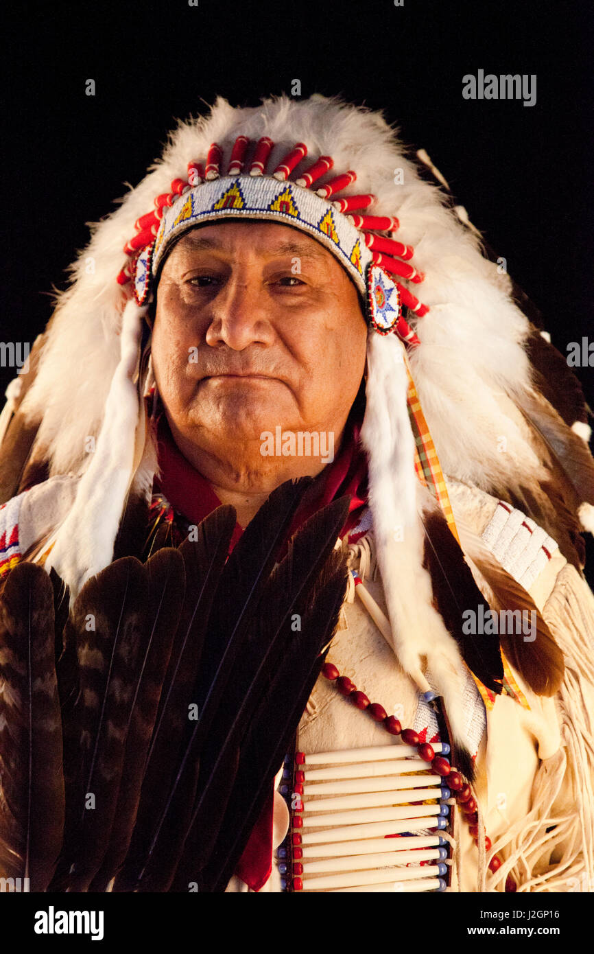 Jonas Grant (Ute, Navajo, Apache) gekleidet in Adler Feder Kopfschmuck Krieg Motorhaube und Hirschleder Jacke mit Perlenstickerei verziert hält ein Tanz-Fan neben einen schwarzen Hintergrund. Stockfoto