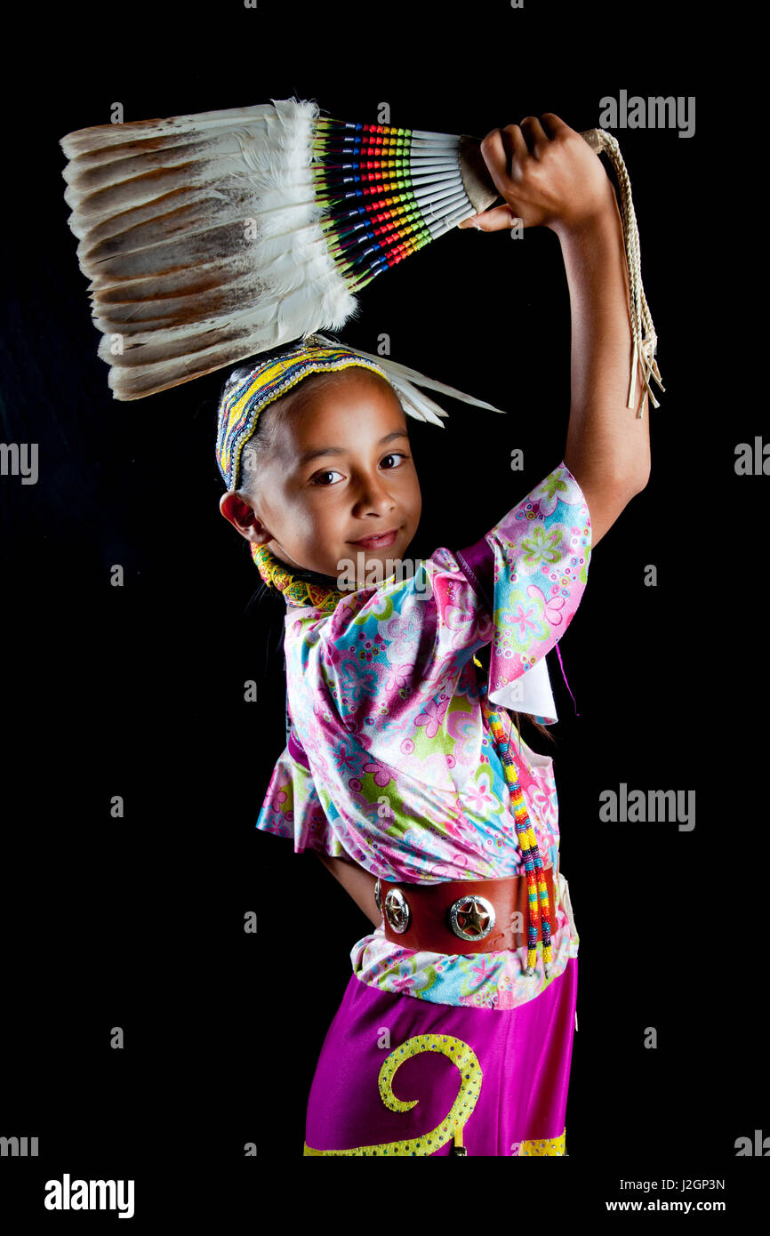 Traditionellen pow Wow Tänzerin 9 Jahre alten Jaydean (Lakota) gekleidet in bunten Insignien und Perlen Haarband ein Feder-Fan vor einem schwarzen Hintergrund hält. Stockfoto