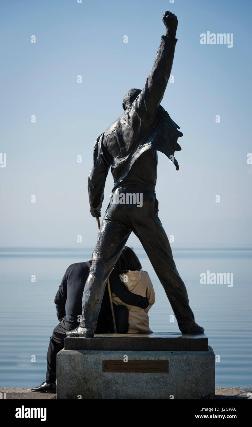 Ein paar sitzt am Fuße der Statue von Freddie Mercury, verstorbenen Sängers der UK-Rock-Band Queen, am Seeufer des Genfer Sees in Montreux, Stockfoto