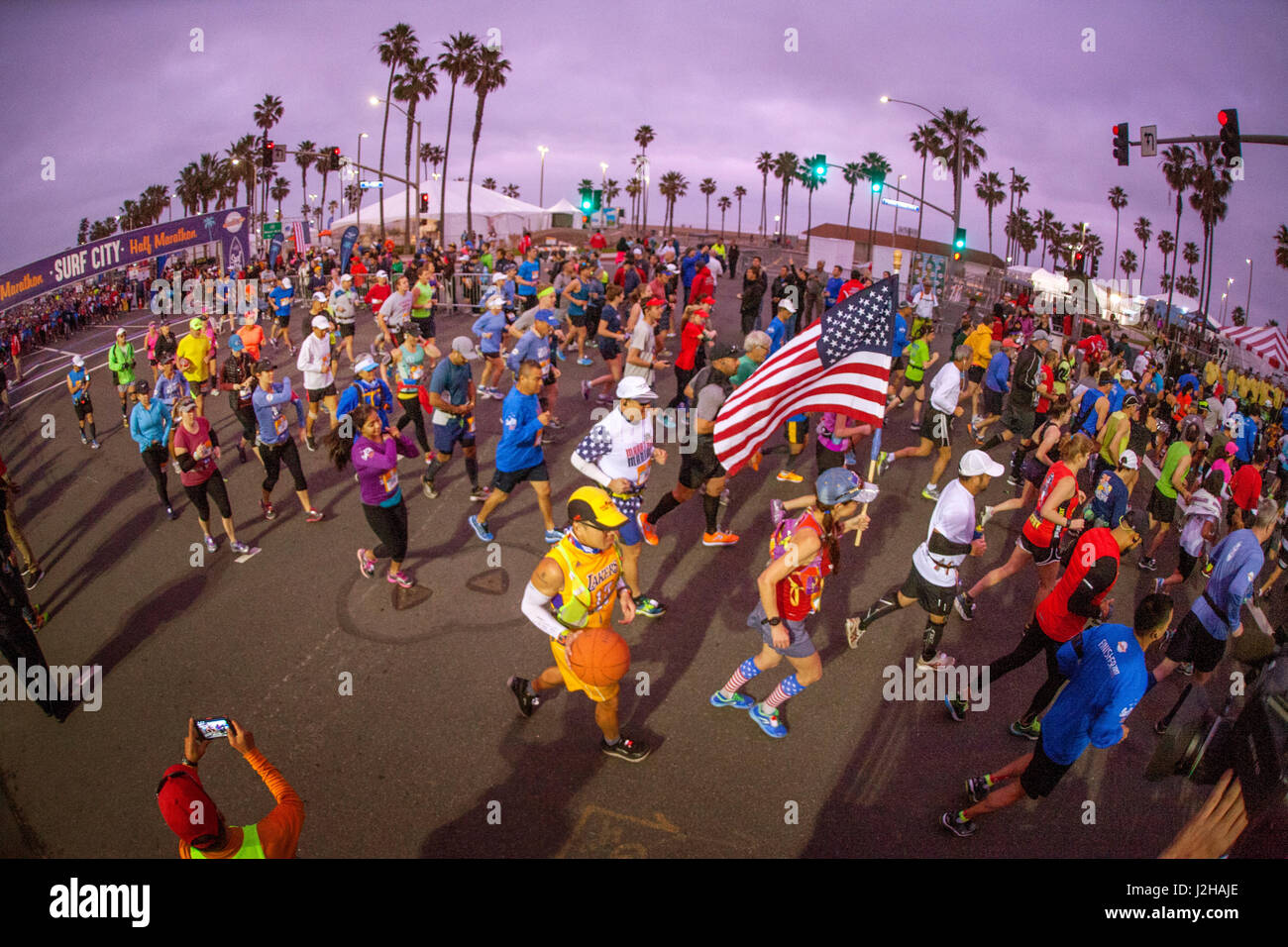 Gemischtrassig Marathon erste Hitze Teilnehmer die Startlinie in Huntington Beach, Kalifornien in den frühen Morgenstunden zu verlassen, umgangssprachlich bekannt als "Surf City." Beachten Sie die amerikanische Flagge von Läufer durchgeführt. Stockfoto