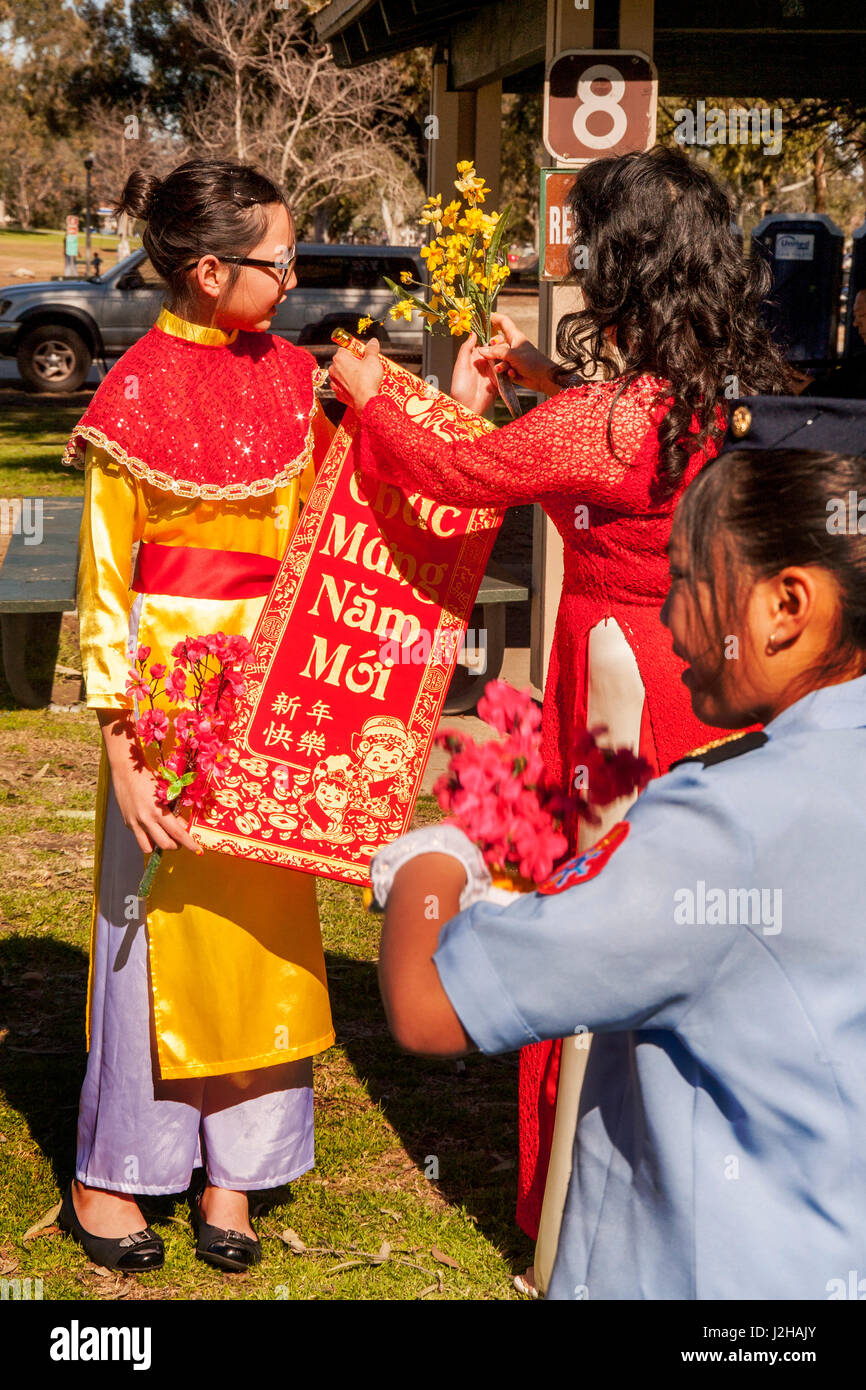 Eine vietnamesische amerikanischen Mädchen in traditionellen Kostümen einen Banner entrollt zu feiern Lunar New Year oder Tet in Fountain Valley, CA, geparkt werden, während eine Mädchen im Vordergrund ein Tanzschritt praktiziert. Stockfoto