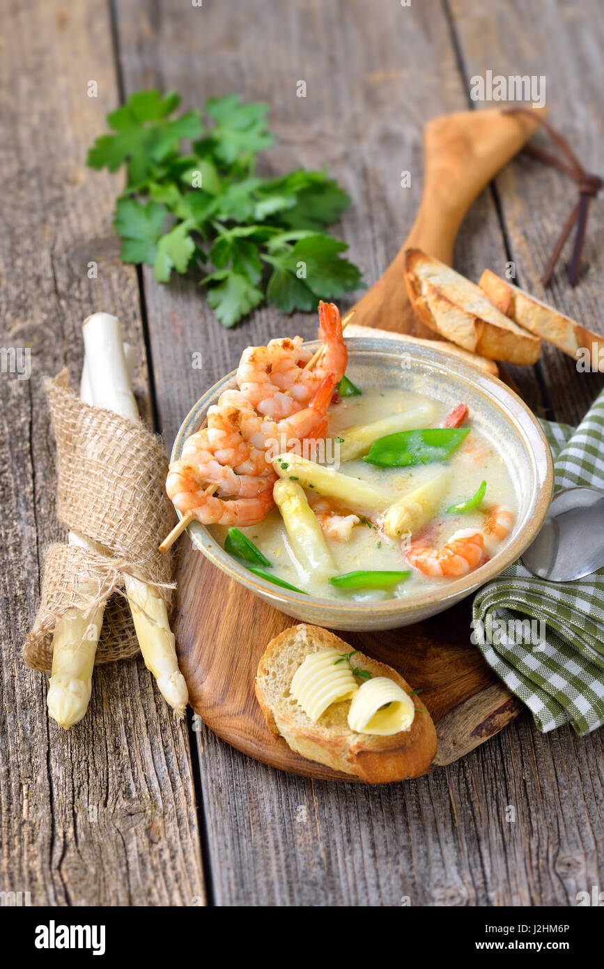 Spargel Suppe mit gebratenen Garnelen und Zuckerschoten, serviert mit geröstetem Baguette mit Butter rollt Stockfoto