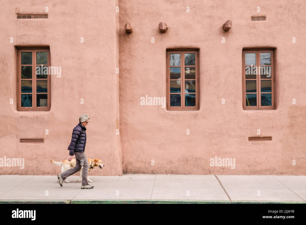 Eine Frau und ihr Hund zu Fuß vor der Adobe-Stil-Haus in Santa Fe, New Mexico Stockfoto