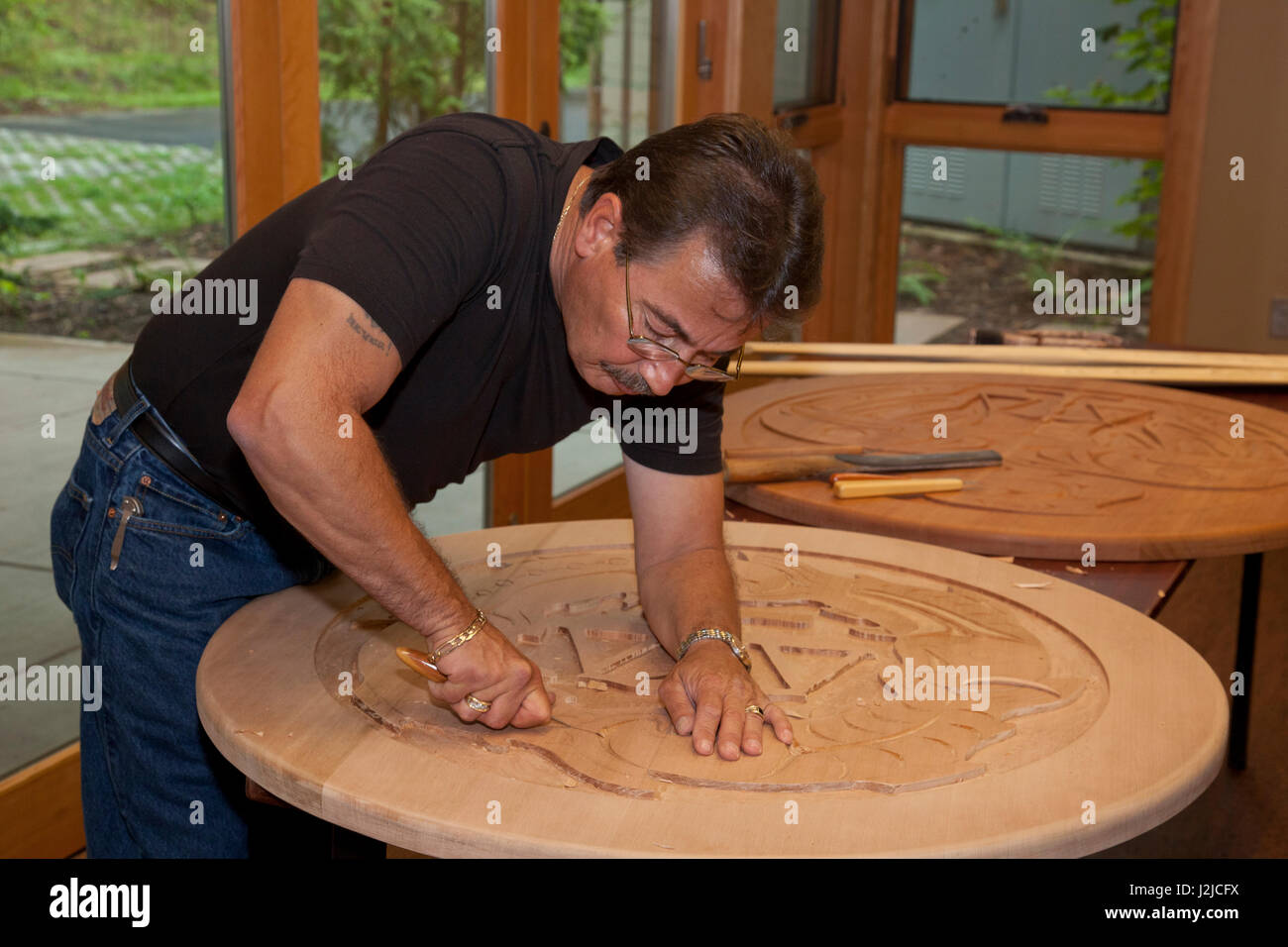 Professional-Küsten-Salish Künstler aus den Stämmen Tulalip gräbt traditionelle Symbole in ein großes Stück des kreisförmigen Zedernholz. Stockfoto