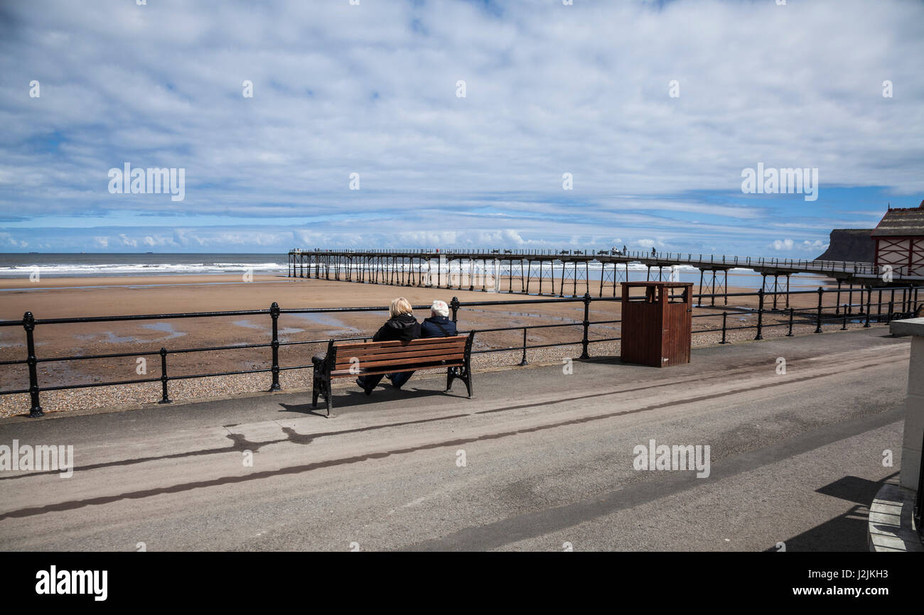 Ein älteres paar sitzen auf einer Bank am Meer, Blick auf den Strand und das Meer am Saltburn am Meer, England, UK Stockfoto