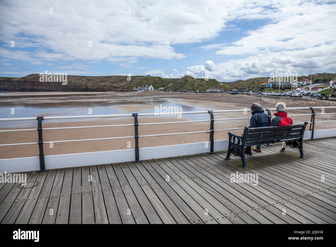 Ein älteres paar sitzen auf einer Bank auf dem Pier, Blick auf Huntcliff, bei Saltburn am Meer, England, UK Stockfoto