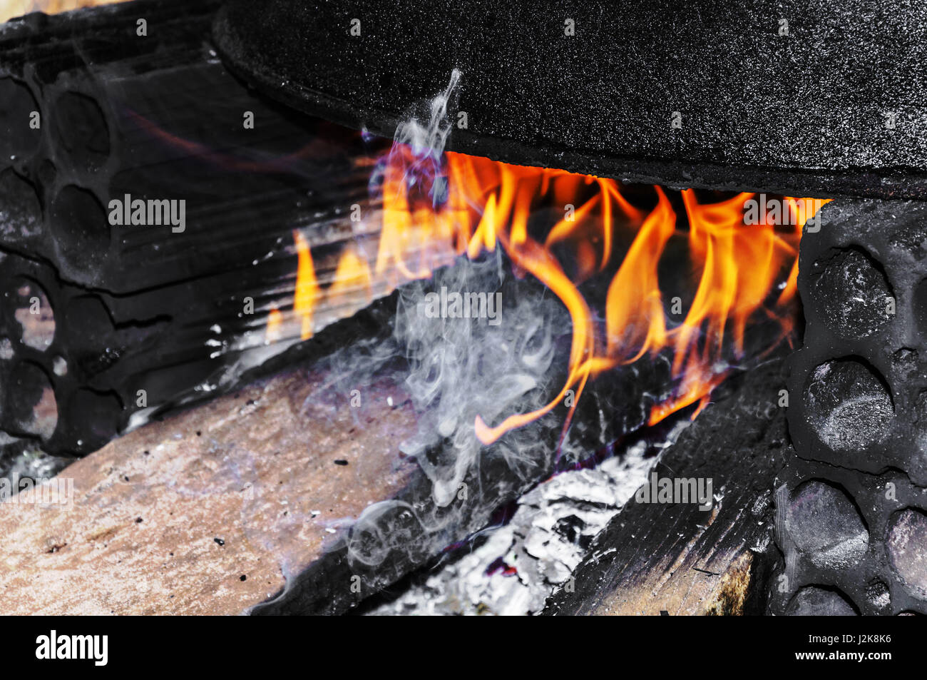 Großen schwarzen Kochtopf auf einem rustikalen Herd improvisiert auf dem Boden. Kochen auf dem Herd mit Ziegeln und Holz hergestellt. Flammen brennen Holz und Rauch her Stockfoto