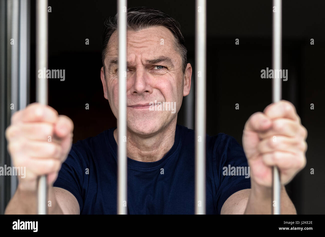 Applying blue eyed Mann inhaftiert und tragen blaues Hemd steht mit Gittern Stockfoto