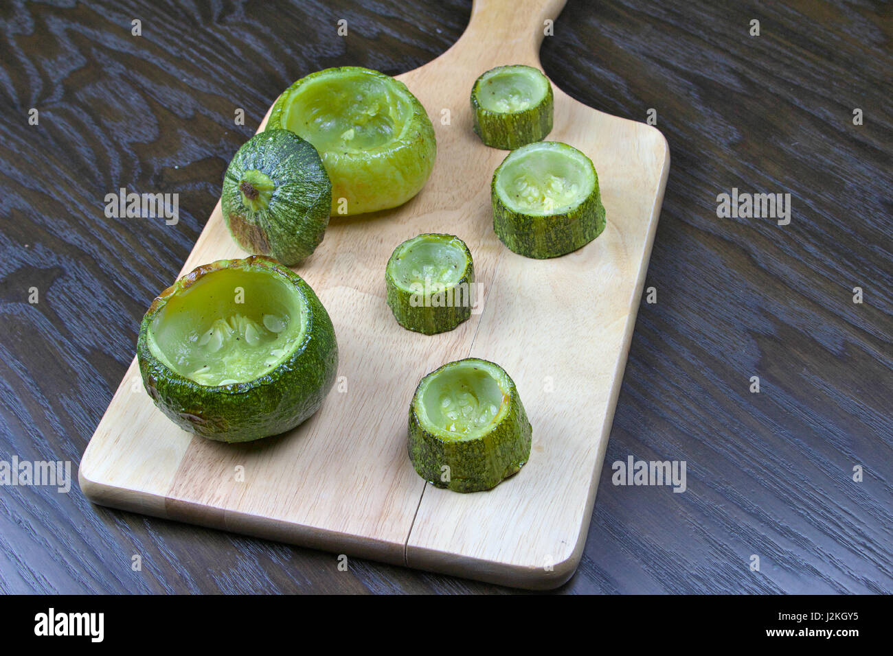 Entleerte Zucchini (Zucchini) auf Holzbrett liegend auf einem dunklen Holztisch - gefüllte Zucchini Rezept Stockfoto