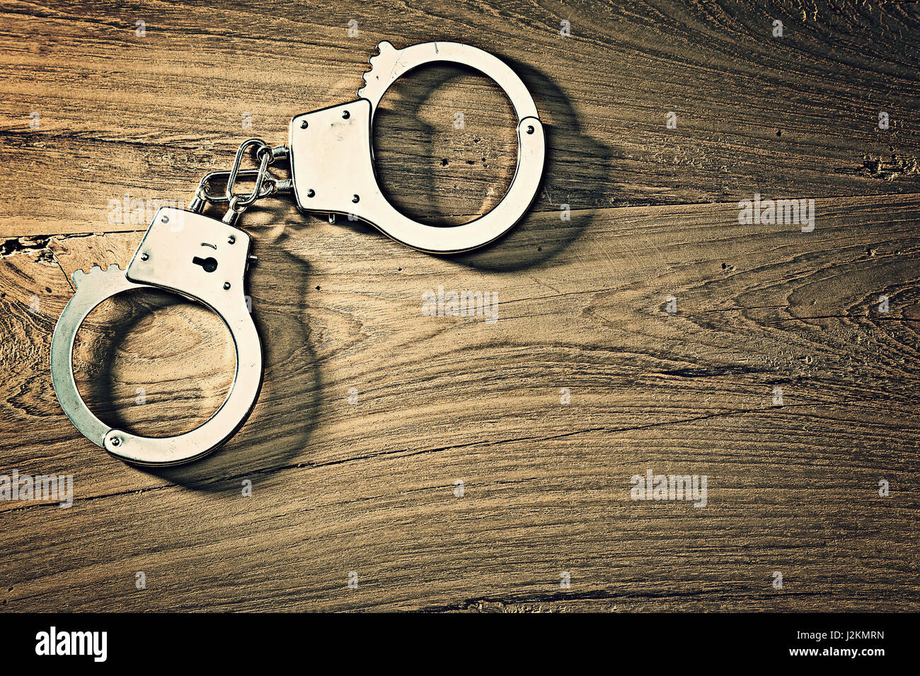 Handschellen auf bewaldeten Tisch in grellem Licht und Farbton, mit rauen und harten Texturen aus Metall und Holz, einsetzbar in Recht und Gerechtigkeit Konzept Stockfoto