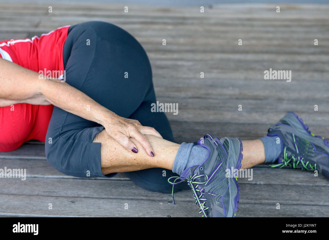 Passen sportliche senior Frau unteren Krämpfe im Bein während des Trainings umklammert ihr Kalb Schmerzen leidet, Nahaufnahme der unteren Körperhälfte liegen auf einem hölzernen Stockfoto