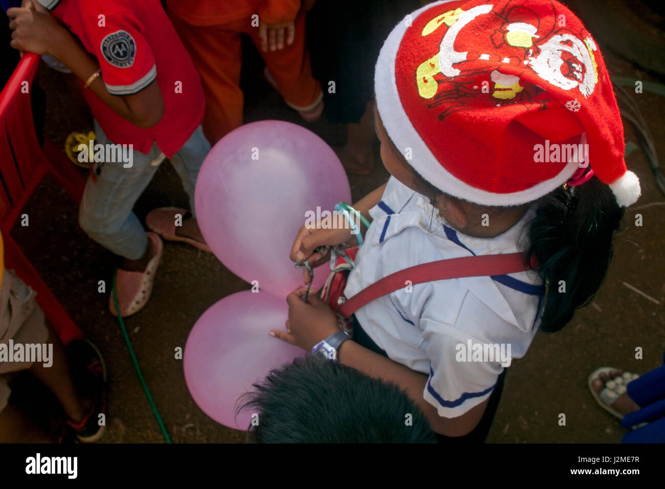 Ein junges Mädchen trägt einen Santa Ckaus Hut haltend Ballons bei der Weihnachtsfeier in einer ausländischen Sprachschule in Tboung Khmom Provinz, Kambodscha. Stockfoto