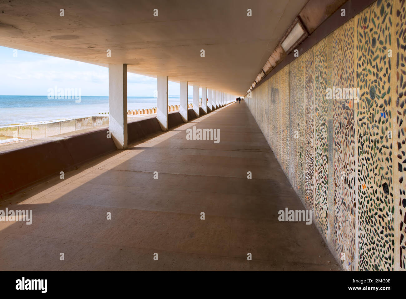 Ein Strand bedeckt konkrete Gehweg mit Mosaik-Muster Wand, Blick auf das Meer zu einer Seite und starken führenden Linien von der Kamera entfernt. Stockfoto