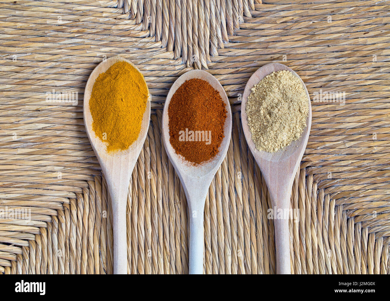 Aufwand für drei Holzlöffel mit Kurkuma, Paprika und Ingwer Gewürz auf Linie-gemusterten Wicker Hintergrund. Stockfoto