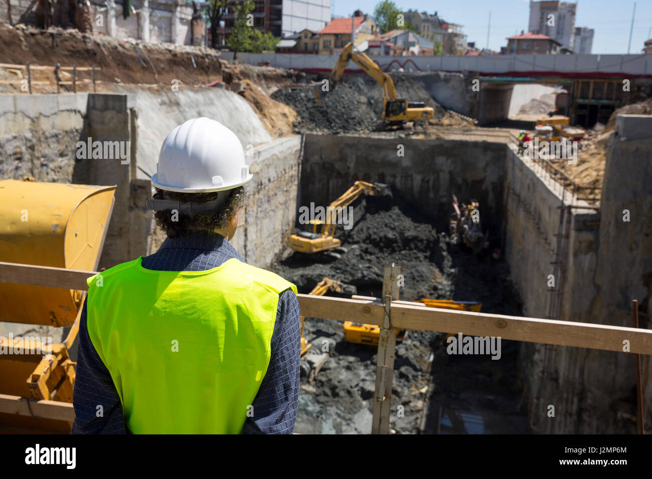 Straße Bauingenieur überwacht Bagger (Bagger) Graben für eine u-Bahn arbeiten. Gekleidet in eine Arbeit einheitlich und schützenden weißen Helm. Von Stockfoto