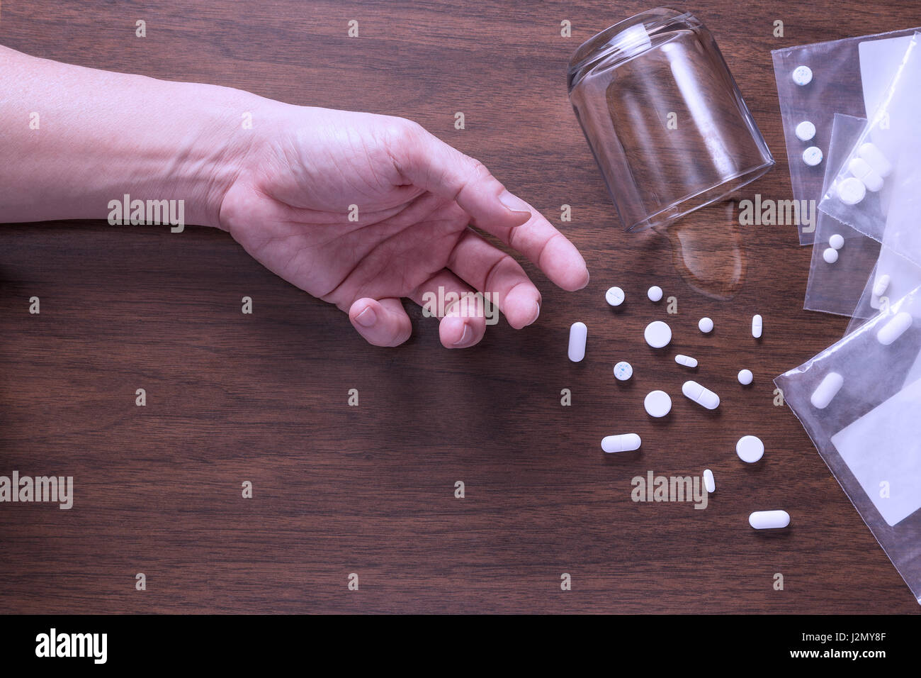 Männliche Hand auf Holzboden mit Spill Drogen und Glas Wasser, Konzept von Überdosierung oder Drogenmissbrauch, mit dunklen Blauton, Traurigkeit und Gefahr Stimmung schaffen Stockfoto