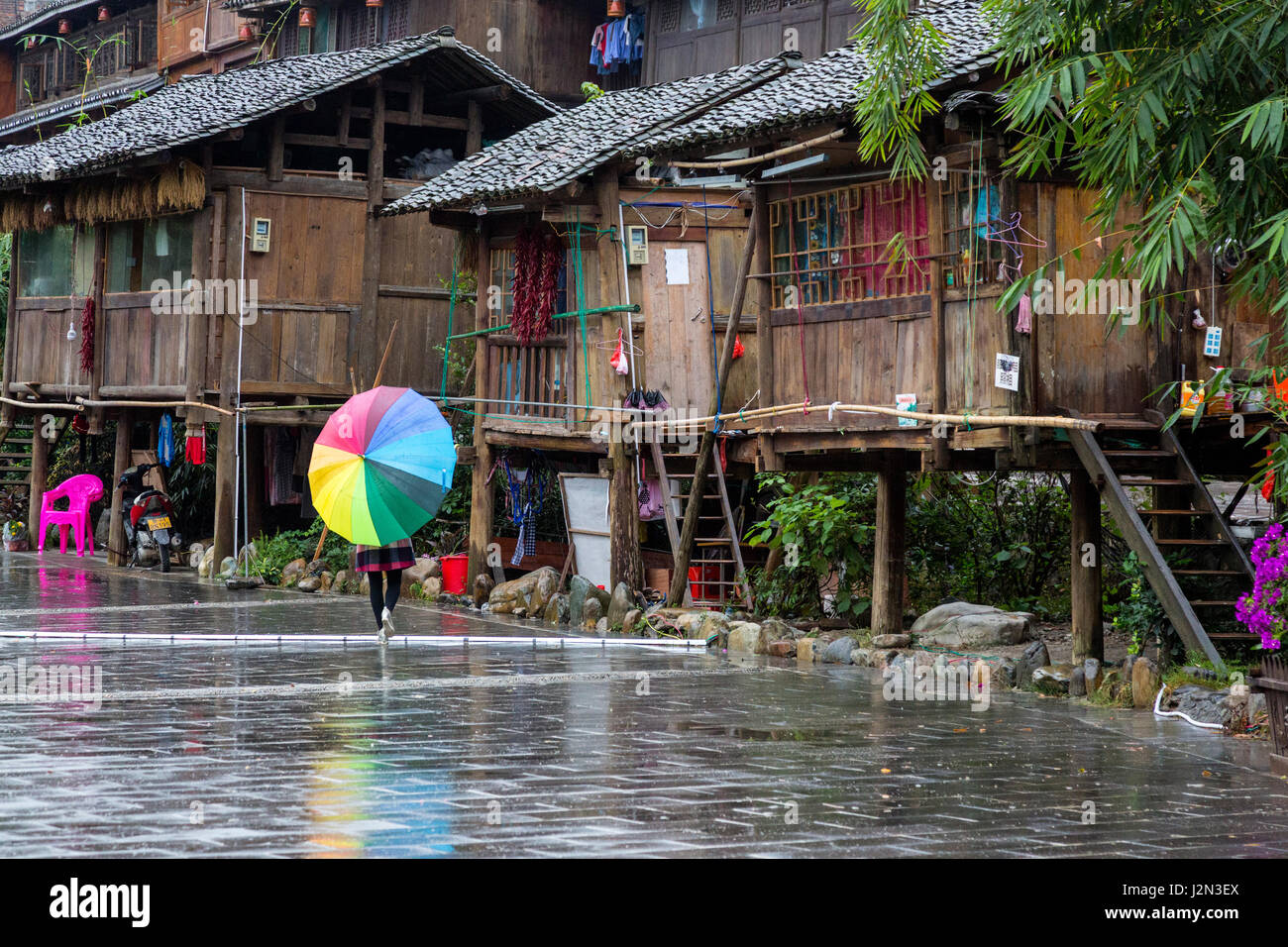 Zhaoxing, Guizhou, China, ein Dong Minderheit Dorf.  Junge Frau mit einem bunten Regenschirm die Straße hinunter. Stockfoto Zhaoxing, Guizhou, China, ein Dong Minderheit Dorf.  Junge Frau mit einem bunten Regenschirm die Straße hinunter. Stockfoto