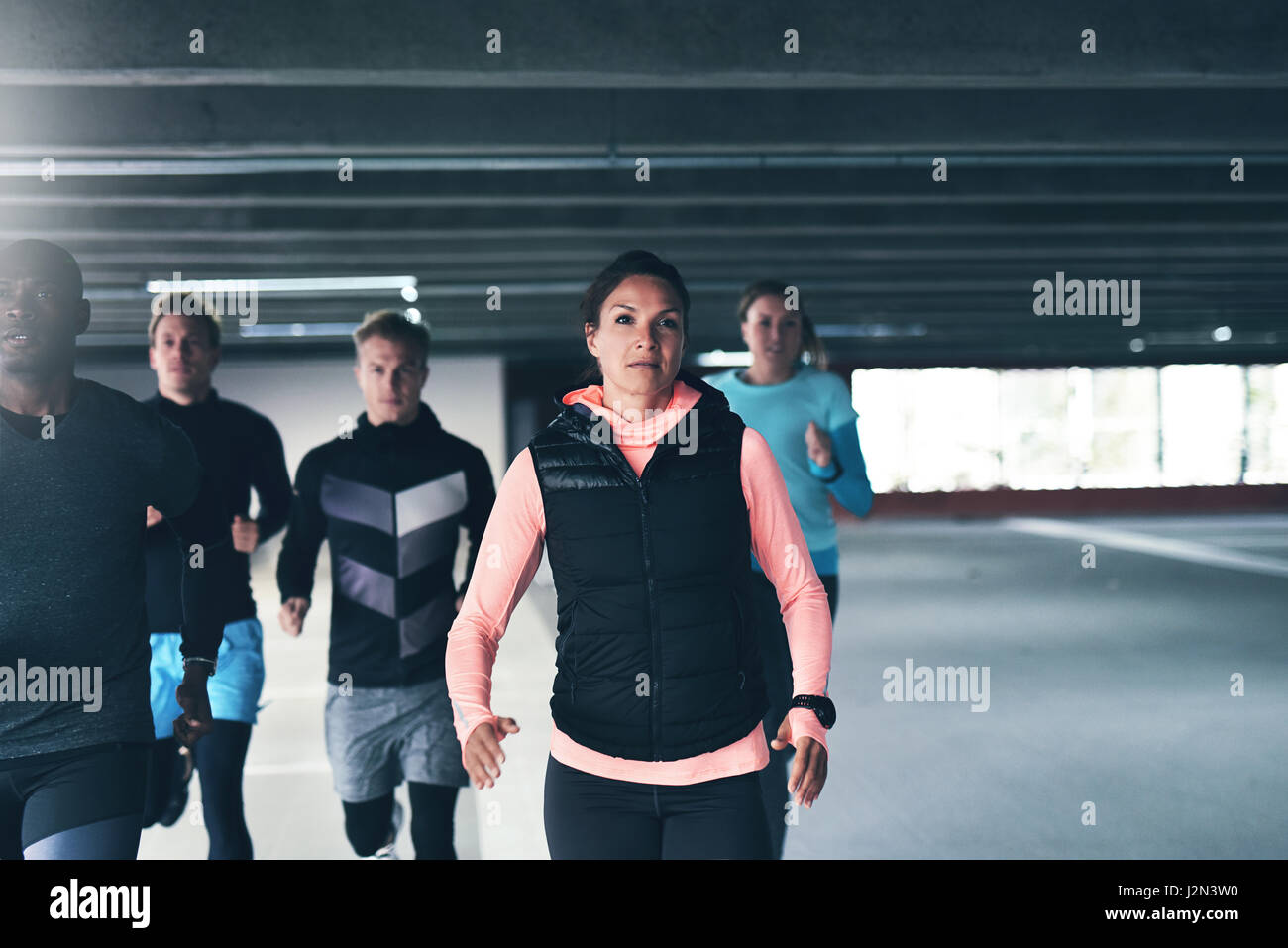 Junge Frau Athlet läuft auf die Kamera, wie sie in einer Tiefgarage mit einer Gruppe von städtischen Freunde trainiert Stockfoto