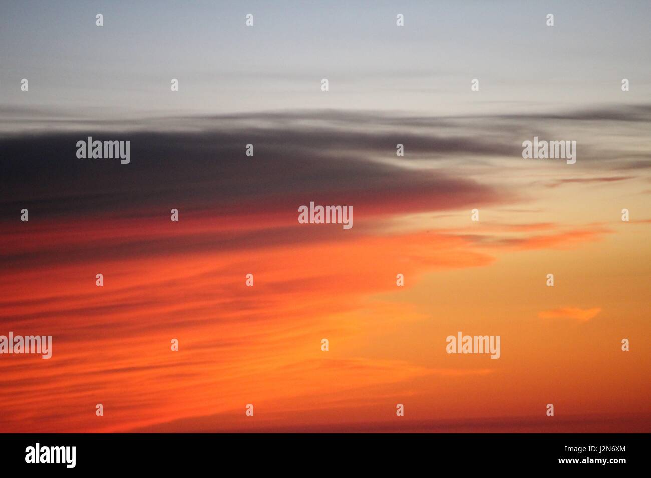 Eine Bank von Wolken beleuchtet eine cremige Orange durch den Sonnenuntergang. Stockfoto