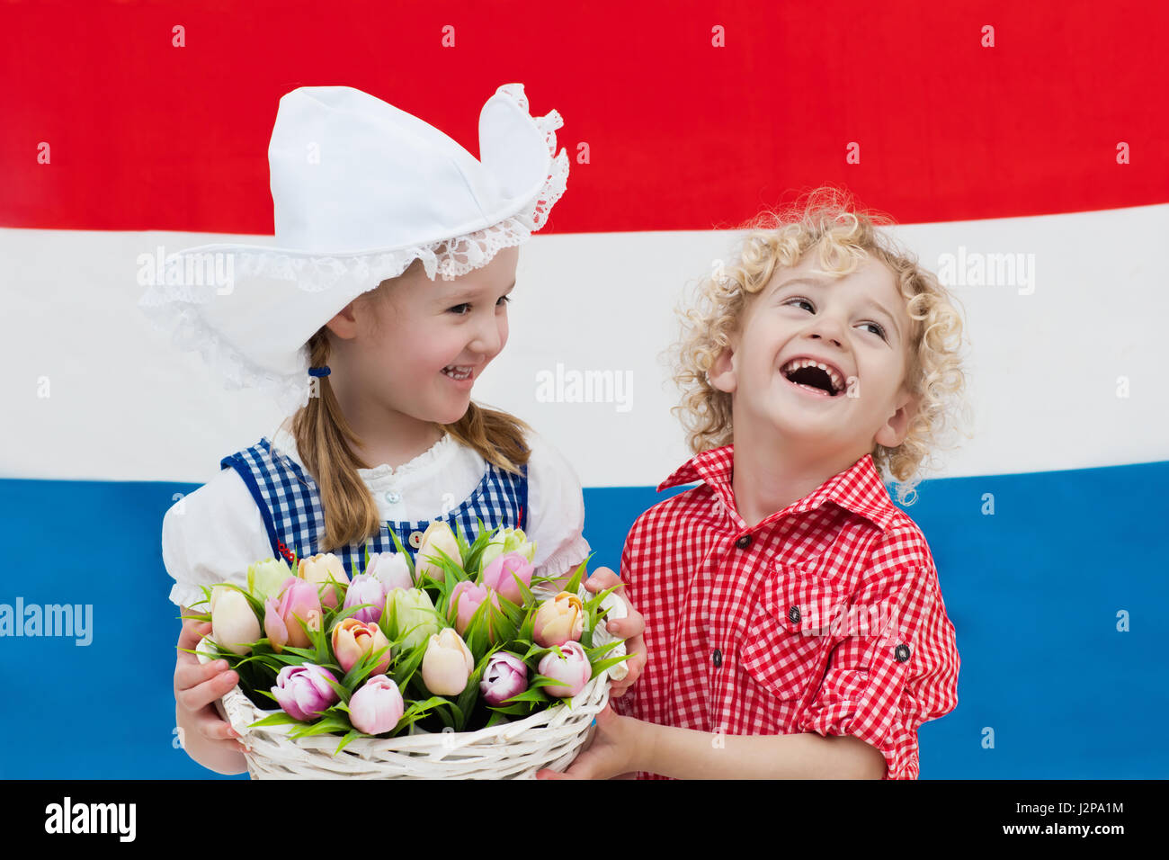 Niederländische Mädchen und jungen tragen traditionelle Tracht, Kleid und Hut Holding Korb mit Tulpen auf der Flagge der Niederlande. Kinder mit souve Stockfoto