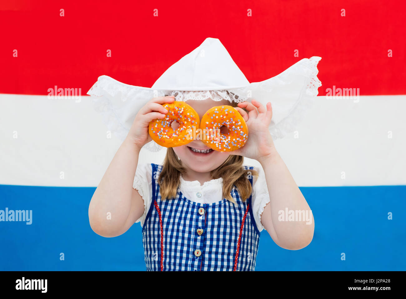 Niederländische Mädchen tragen traditionelle Tracht, Kleid und Hut hält orange Donuts auf der Flagge der Niederlande. Kind mit Oranje Souvenirs fr Stockfoto