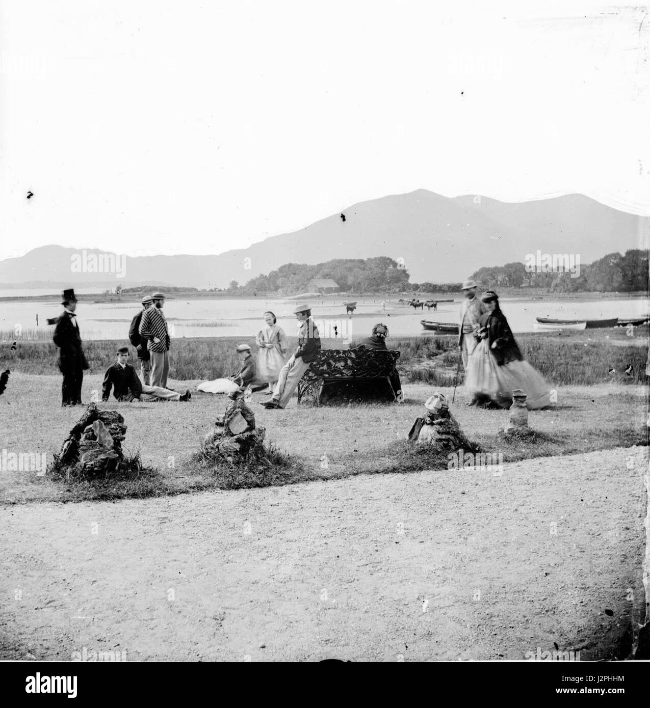 Gruppe von zehn Personen stehend und liegend auf einer Insel oder Halbinsel, mit Hügeln im Hintergrund. Stockfoto