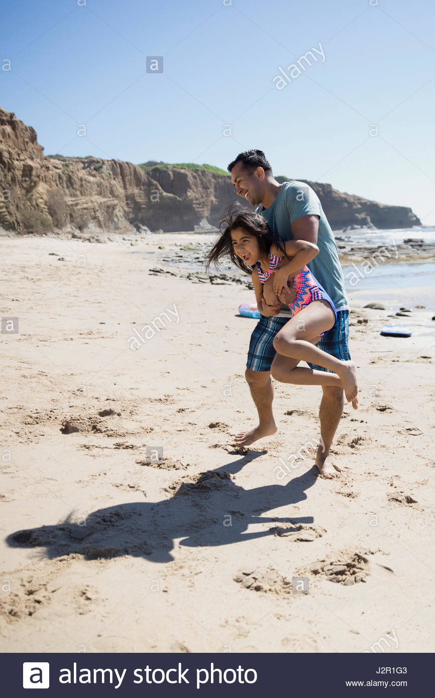 Latino-Vater mit Tochter am sonnigen Strand spielen Stockfoto