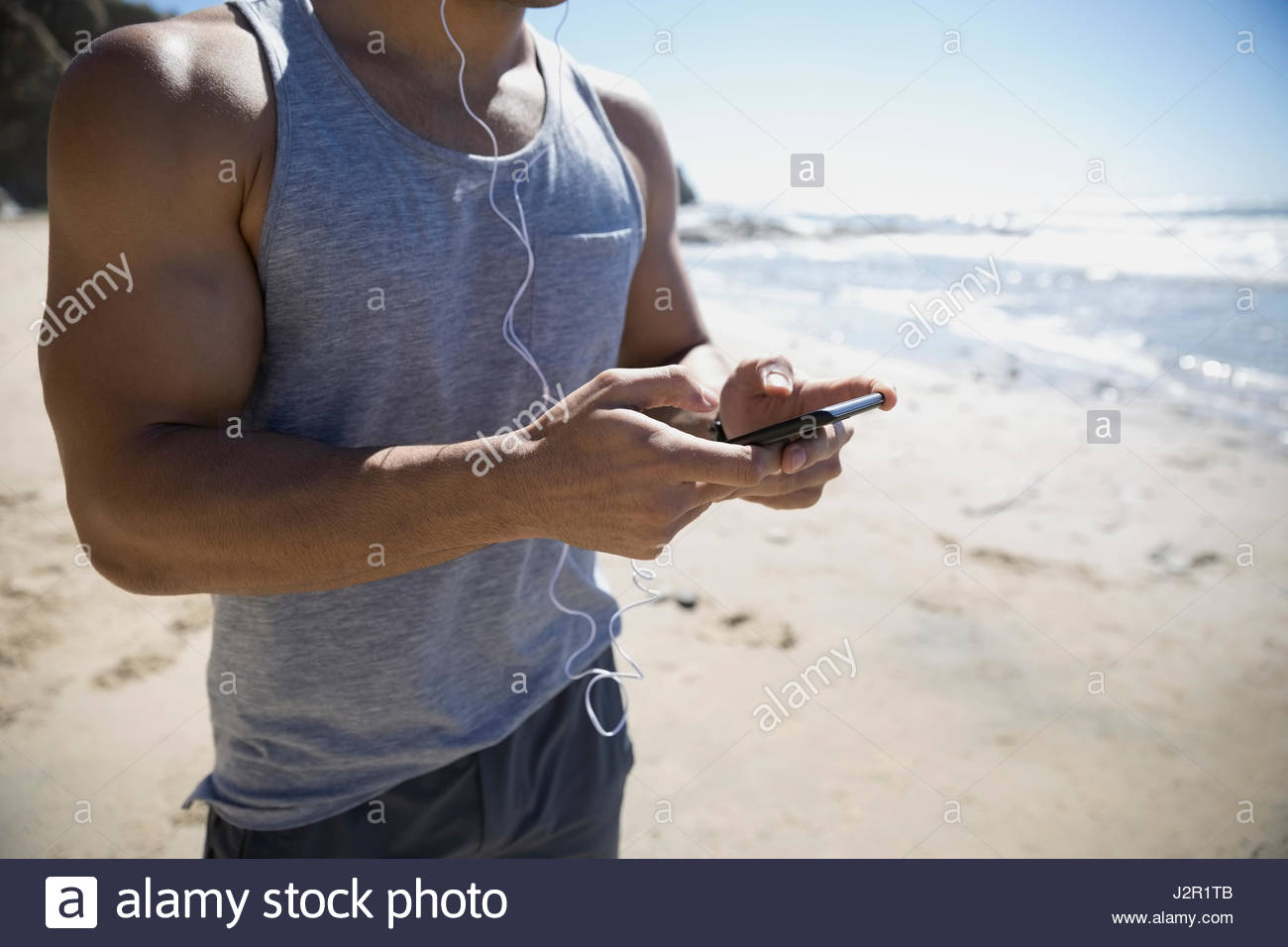 Junge männliche nahöstlichen Läufer Musikhören mit MP3-Player und Kopfhörer am Sonnenstrand Stockfoto