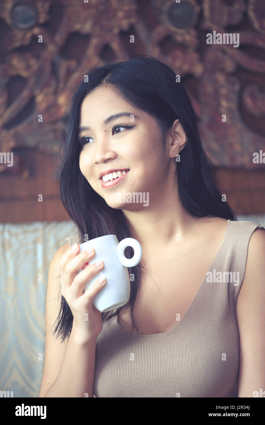 Asiatische Frau hält eine Tasse Kaffee mit Blick hinter der Kamera Stockfoto