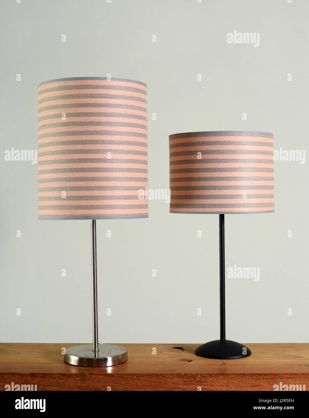 Zwei verschiedene Stil Metall-Lampen mit passenden gestreifte zylindrische Schattierungen auf einem Holztisch vor einer grünen Wand stehend Stockfoto