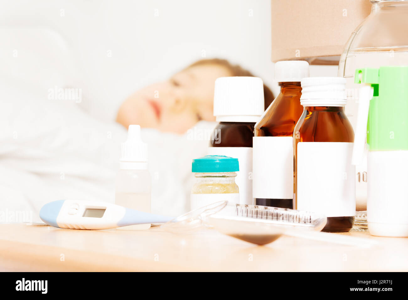 Nahaufnahme Bild des elektronischen Thermometer und Medikamente Flaschen mit ausgeblendeten Beschriftungen auf Bett-Tisch für die Behandlung der Kranken jungen Stockfoto