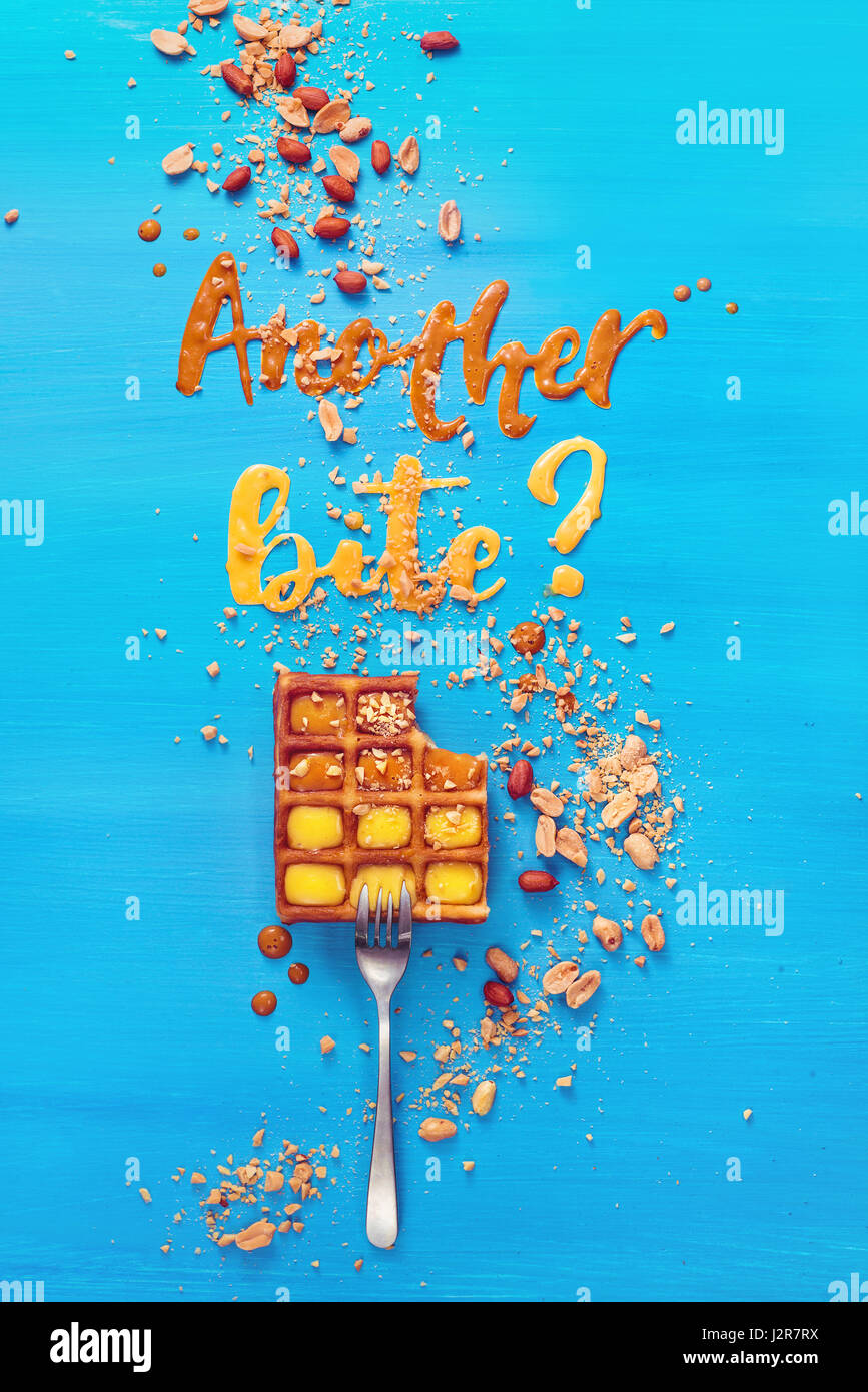 Eine Gabel mit belgischen Waffeln auf einem himmelblauen hölzernen Hintergrund mit Worten machte einen weiteren Bissen mit Karamell und Erdnuss-Sirup Stockfoto