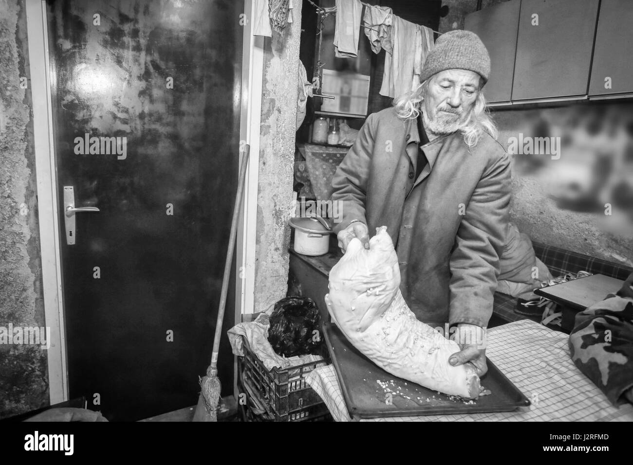 Ein Alter Mann, ein großes Stück Schweinefleisch würzen und bereitet sie für den Ofen. Stockfoto